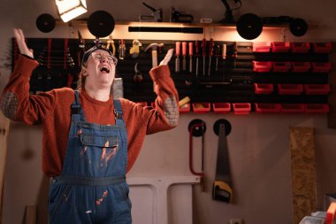 Tamir atölyesinde çalışırken iş yerinde gözlüklü ve tulumlu sinirli kadın tamirci. Boşluğu kopyala