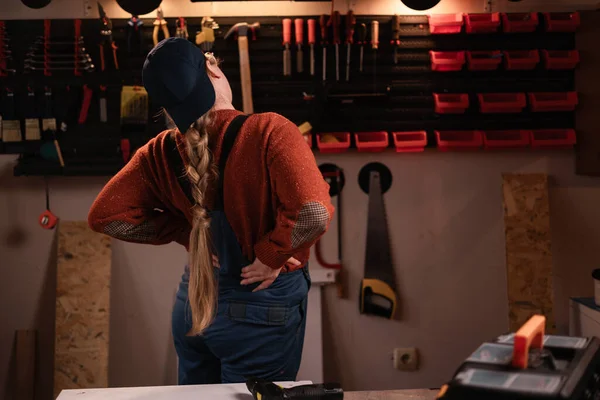 Tulumlu ve gözlüklü kadın tamirci tamirhanede çalışırken sırtı ağrıyormuş. Boşluğu kopyala