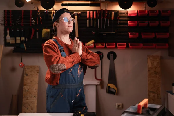 İş tulumlu ve gözlüklü kadın tamirci tamirhanede çalışırken iyi haberler için dua ediyor. Boşluğu kopyala