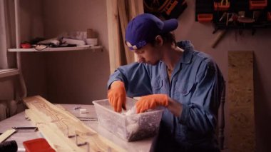 Odaklanmış tamirci iş sırasında plastik bir düzenleyicide metal vidalar ve bağlayıcılar arıyor. Erkek teknisyen, küçük bir atölyede tamir projesi için donanım parçaları seçiyor.