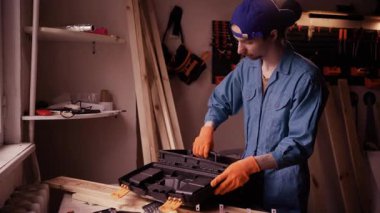 Üniformalı profesyonel bir tamirci iş ekipmanlarını düzenliyor ve alet çantasına anahtar koyuyor. Tamirci, garajda ya da bakım servisinde işini bitiriyor.