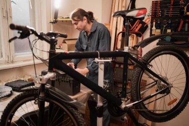 Bisiklet tamircisi atölyede bozuk bisikleti ayarlıyor. Boşluğu kopyala