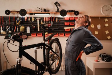 Bisiklet tamiri ve bakım atölyesinde. Hasta bisiklet tamircisinin sırt ağrısı var. Bisikletle çalışırken sırt ağrısı çekiyor. Boşluğu kopyala