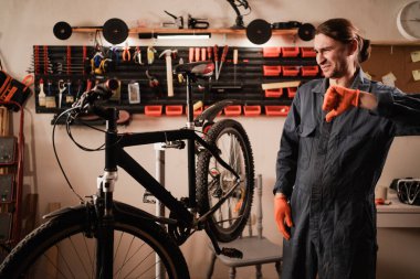 Hoşlanmamak. Bisiklet tamiri ve bakım atölyesinde. Bisiklet tamircisi bisiklet tamirinde çalışırken baş parmağıyla işaret dilini gösteriyor. Boşluğu kopyala