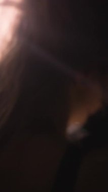 Yüzü ve saçlarını aydınlatan parlak bir ışığa sahip bir kadının yakın plan portresi karanlıkta çok güzel bir kontrastlık yaratıyor. Güzellik, duygusallık, ruh hali. dikey video