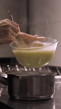 Hamur işi şefinin yumurta sarısı karışımını ev yapımı eklerlere krema doldurmak için sıcak sütle bir tencereye karıştırmasını kapatın. dikey video