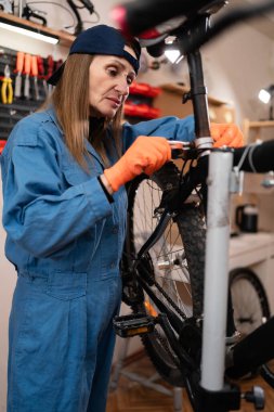 Bisiklet dükkanında teknik uzmanlık. Orta yaşlı bayan bisiklet tamircisi atölyede bir bisikleti tamir ediyor. Boşluğu kopyala