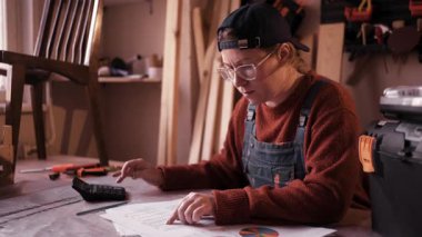 İş harcamalarını hesaplayan ve atölyesindeki muhasebe belgelerini yöneten profesyonel kadın marangoz. Küçük işletme yönetimi, girişim finansmanı ve girişimcilik kavramı.