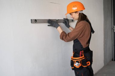 Ev yenileme çalışmaları sırasında ruh seviyesini kullanarak beton duvar ölçen kadın inşaat işçisi ya da inşaat işçisi. Boşluğu kopyala