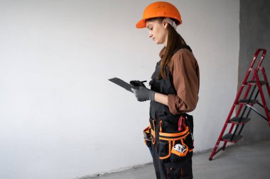 Kadın müteahhit. Şapkalı ve üniformalı bir kadın. Elinde pano var. Restorasyon dairesi projesinde çalışıyor. İnşaat, meslek ve ev yenileme konsepti