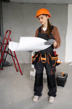 Profesyonel kadın mimar ya da inşaatçı üniformalı ve ev inşaatının planlarını elinde tutuyor ve yenilemeyi planlıyor. Onarım, inşaat ve inşaat kavramı.