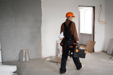 Alet çantası yürüyüşü yapan kadın tamirci tamamlanmamış binaya giriyor. Yenileme dairesi aletleri. Ev konseptini onar