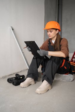 Kadın tamirci, ustabaşı ya da üniformalı ya da inşaatçı elinde pano ve tadilat planı tutan. Onarım, inşaat ve inşaat konsepti. Boşluğu kopyala