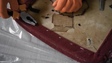 Eski ahşap sandalyeden eski döşemeleri çıkarmak için pense kullanarak mobilyacı ellerini kapat. Bir atölyede profesyonel mobilya restorasyon süreci ve antika yenileme konsepti.