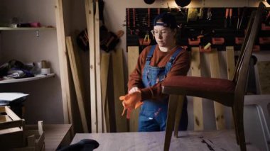 Bayan mobilya restoratörü yenileme atölyesinde çalışmadan önce turuncu koruyucu eldiven giyiyor. Mobilya restorasyonu kavramı