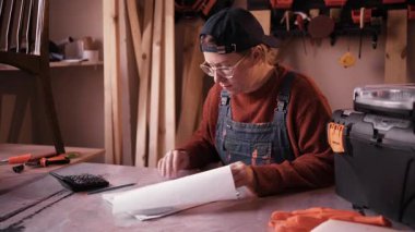 Küçük işletme finansmanlarını hesap makinesiyle yöneten, başlangıç giderlerini hesaplayan ve atölyedeki muhasebe belgelerini yöneten kadın marangoz. Küçük işletme yönetimi kavramı, mali planlama