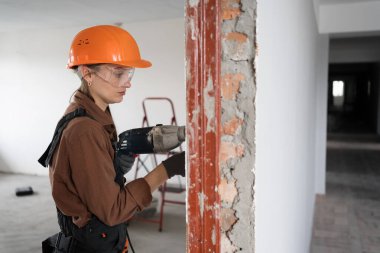 Çekiç matkabı kullanan kadın inşaat işçisi. Havalı çekiç matkaplı kadın duvarda delik açıyor. Boşluğu kopyala