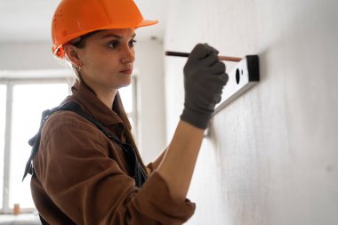 Ev yenileme çalışmaları sırasında ruh seviyesini kullanarak beton duvar ölçümleri yapan kadın inşaat işçisi. Boşluğu kopyala