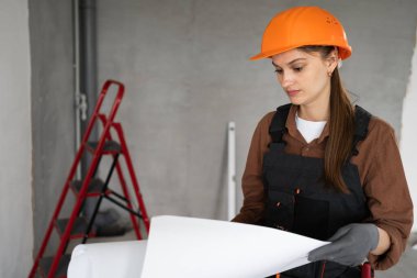 Profesyonel kadın mimar ya da inşaatçı üniformalı ve ev inşaatının planlarını elinde tutuyor ve yenilemeyi planlıyor. Onarım, inşaat ve inşaat kavramı.