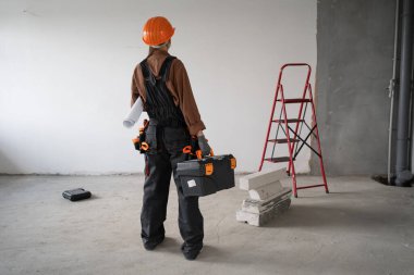 Alet çantası yürüyüşü yapan kadın tamirci tamamlanmamış binaya giriyor. Yenileme dairesi aletleri. Ev konseptini onar