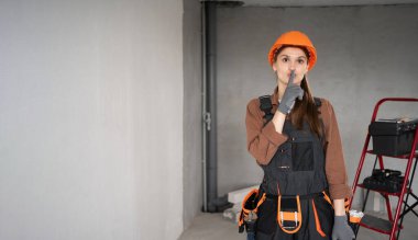 Kadın Mimar. İş tulumlu kadın mimar ve yarım kalmış bir binada sessiz ol, sessiz ol, sessiz ol, jest yap. Onarım, inşaat ve inşaat konsepti. Pankart. Boşluğu kopyala