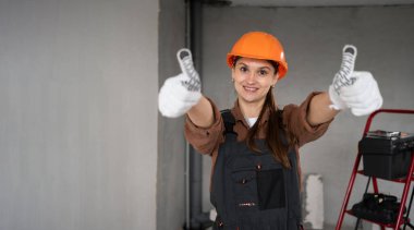 Kadın Mimar. İş tulumları içinde mutlu bir kadın mimar ve bitmemiş bir binada baş parmak hareketi gibi iyi bir izlenim bırakıyor. Onarım, inşaat ve inşaat konsepti. Pankart. Boşluğu kopyala