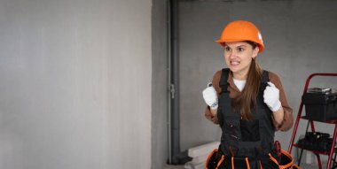 Kadın Mimar. Kızgın agresif kadın mimar iş tulumları ve bitmemiş binada öfke jesti tutuyor. Onarım, inşaat ve inşaat konsepti. Pankart. Boşluğu kopyala