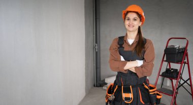 Kadın Mimar. İş tulumlu kadın mimar portresi ve bitmemiş binadaki kameraya bakan kasket. Onarım, inşaat ve inşaat konsepti. Pankart. Boşluğu kopyala