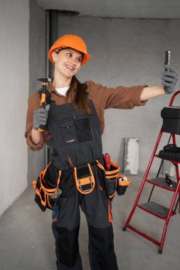 Kadın Mimar. Kadın mimar binada çekiçle selfie çekiyor. Mimar portresi. Bitmemiş binada çalışan üniformalı bir mimar. Boşluğu kopyala