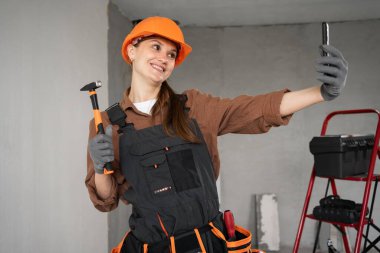 Kadın Mimar. Kadın mimar binada çekiçle selfie çekiyor. Mimar portresi. Bitmemiş binada çalışan üniformalı bir mimar. Boşluğu kopyala