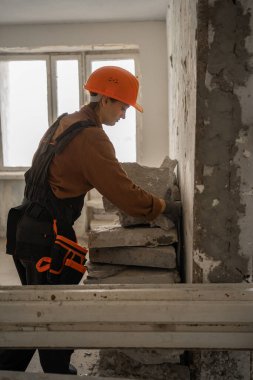 Üniformalı çalışkan kadın müteahhit ev onarımından önce inşaat atıklarını ve çöpleri odadan temizliyor. Ev geliştirme projesi için iç mekanı temizleyen profesyonel kadın işçi..