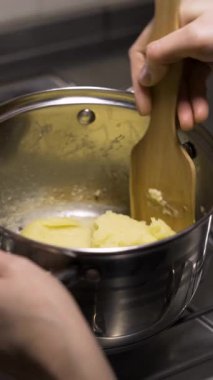 Ahşap bir spatula kullanarak kalın hamur işlerini metal bir tencerede karıştıran bir şefin ev yapımı eklairleri adım adım yapma işlemini kapat. dikey video