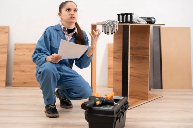 İş yerinde çalışan bir kadın mobilya panellerini birleştiriyor ve el kitabı okuyor. Mobilya montajı. Boşluğu kopyala