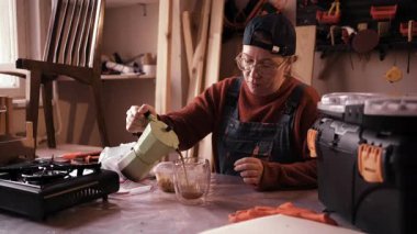 Bayan marangoz öğle yemeği molasında ve marangoz atölyesinde kahve dolduruyor. Boşluğu kopyala