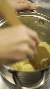 Bir hamur işi şefinin, ahşap bir spatula kullanarak, kalın sarı kremayı metal bir tencerede karıştırarak geleneksel eklem ya da pastalar için doldurma hazırlayan kapağını kapatın..