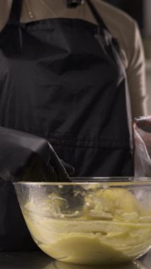 Koyu ev yapımı choux hamuru plastik bir torbaya koymak için spatula kullanan bir pasta şefinin kapağını kapat, adım adım eklerleri pişirmeye hazırlan..