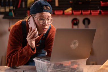 Profesyonel bir marangoz garajındaki marangozluk aletlerini kullanarak ahşap ile çalışır, telefonla konuşur ve verileri bir dizüstü bilgisayara girer. El işi, yaratıcı küçük işletme.