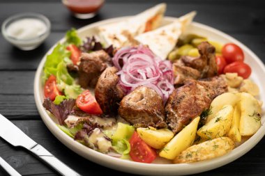 Patates dilimleri ve sebzelerle servis edilen sulu kavrulmuş et şişleri. Yemek menüsü ya da yemek servisi için nefis bir barbekü yemeği. Restoran menüsü kavramı.