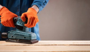 Tahta bir yüzeyi pürüzsüz kılmak için erkek ellerinin titreşim yörüngesi zımparalayıcısını kullan. Ahşap işleme ve DIY ev geliştirme konsepti. Metin için boşluk