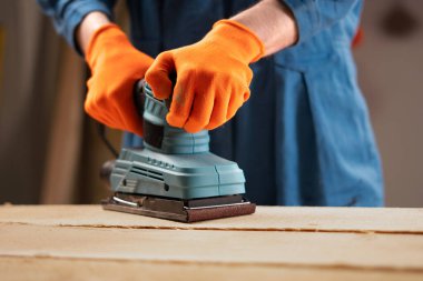 Erkek marangoz, mobilya üretim atölyesinde zımpara makinesi tutuyor. yakın plan