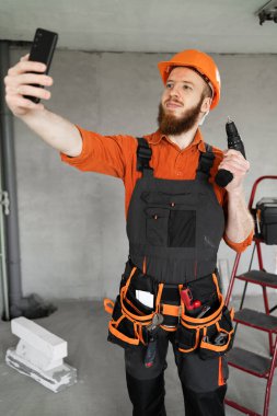 Elinde matkap olan koruyucu şapkalı bir tamircinin portresi. Meslek, inşaat ve inşaat konsepti