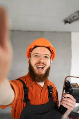 Turuncu kasketli inşaat işçisi akıllı telefon kamerasıyla selfie çekiyor. POV