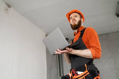 Bilgisayar kullanarak üniformalı ve kasklı müteahhit. İnşaat ve ev yenileme konsepti. Boşluğu kopyala