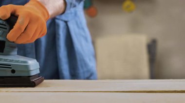 Turuncu eldivenli, elektrikli zımpara makinesiyle çalışan erkeklerin yakın çekimi. Boşluğu kopyala