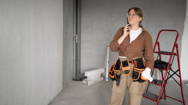 Alet kemeri takan kadın müteahhit telefonda müşteriyle konuşuyor. Onarım, inşaat ve inşaat kavramı