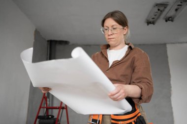 İnşaat işçisi inşaat alanında ya da yenileme dairesinde çalışan kağıt planları okuyor. Boşluğu kopyala