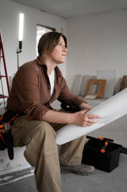 İnşaat halindeki bir evin zemininde oturan kadın müteahhit ya da iç mimar, kat planları ve ev yenileme projesinin planları üzerinde çalışıyor ve tadilat yapıyor..