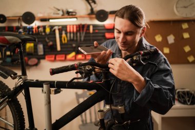 Cep telefonu konuşma hoparlörlü erkek motor tamircisi bisiklet dükkanında ya da garajda çalışan akıllı telefondan sesli mesaj kaydediyor. Boşluğu kopyala