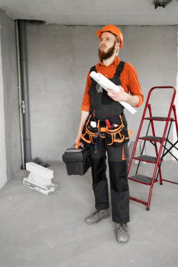 Tamir edilmeden önce taslak ve alet çantasıyla yeni bir daire arayan kasklı ve tulumlu bir tamirci. Boşluğu kopyala