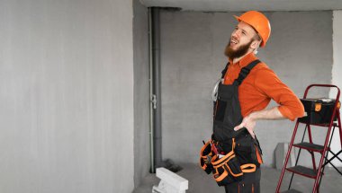 Kasklı sağlıksız müteahhit binanın arka planında sırt ağrısı çekiyor. Sağlık, inşaat ve onarım konsepti. Pankart. Boşluğu kopyala